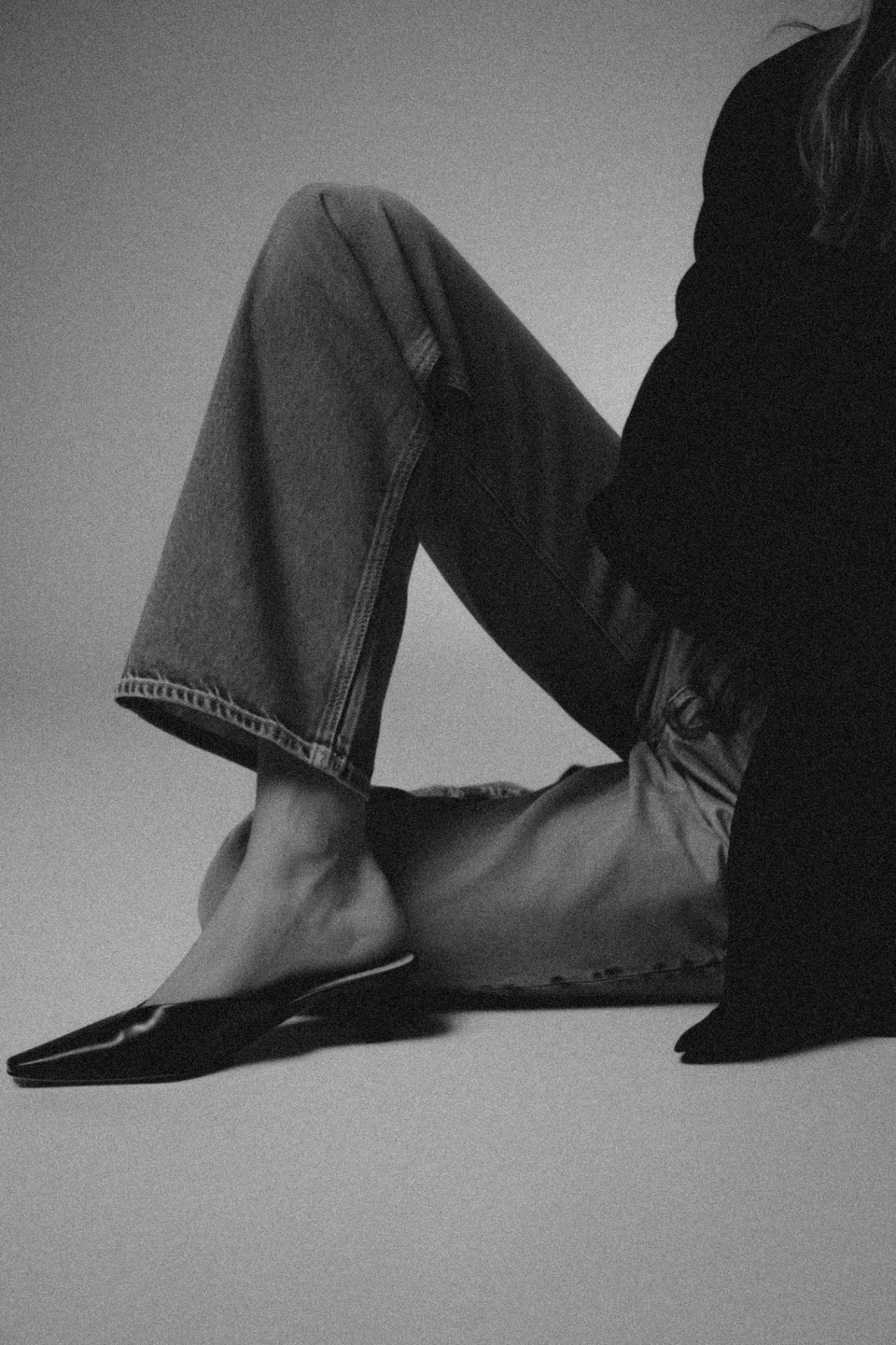 Black and white editorial portrait of crossed legs in denim and black leather flats
